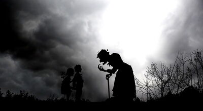 A silhouette of a witch and two kids at night